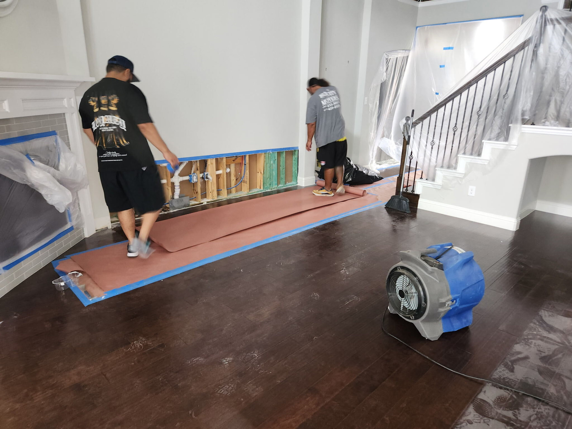 Restoration crew working around an opened interior wall with drying equipment nearby